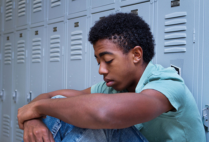 Sad looking teenager sat against lockers in school