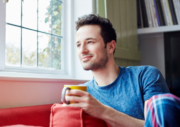 Man holding cup looking out window