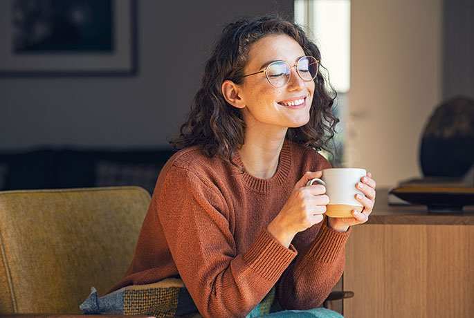 Young woman sitting enjoying a cup of tea smiling happily